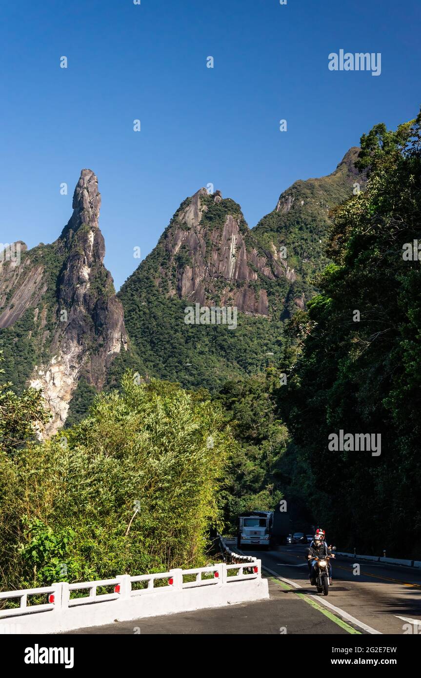 Traffic climbing the narrow Rio-Teresopolis highway nearby Soberbo viewing spot with God's Finger and Cabeca de Peixe (Fish Head) peaks at the back. Stock Photo