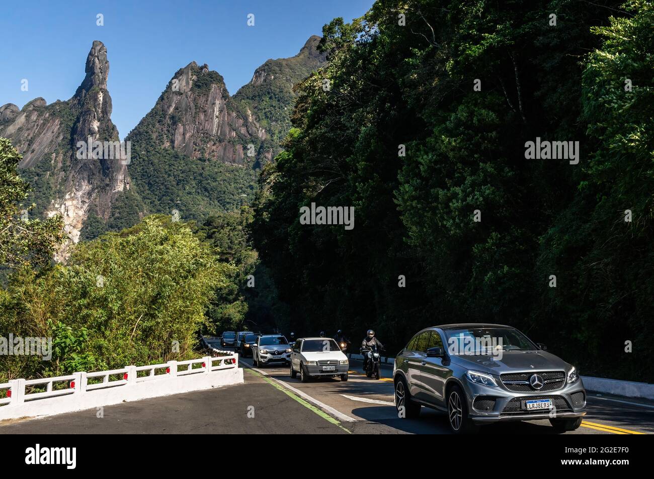 Cars climbing the narrow Rio-Teresopolis highway nearby Soberbo viewing spot with God's Finger and Cabeca de Peixe (Fish Head) peaks at far back. Stock Photo
