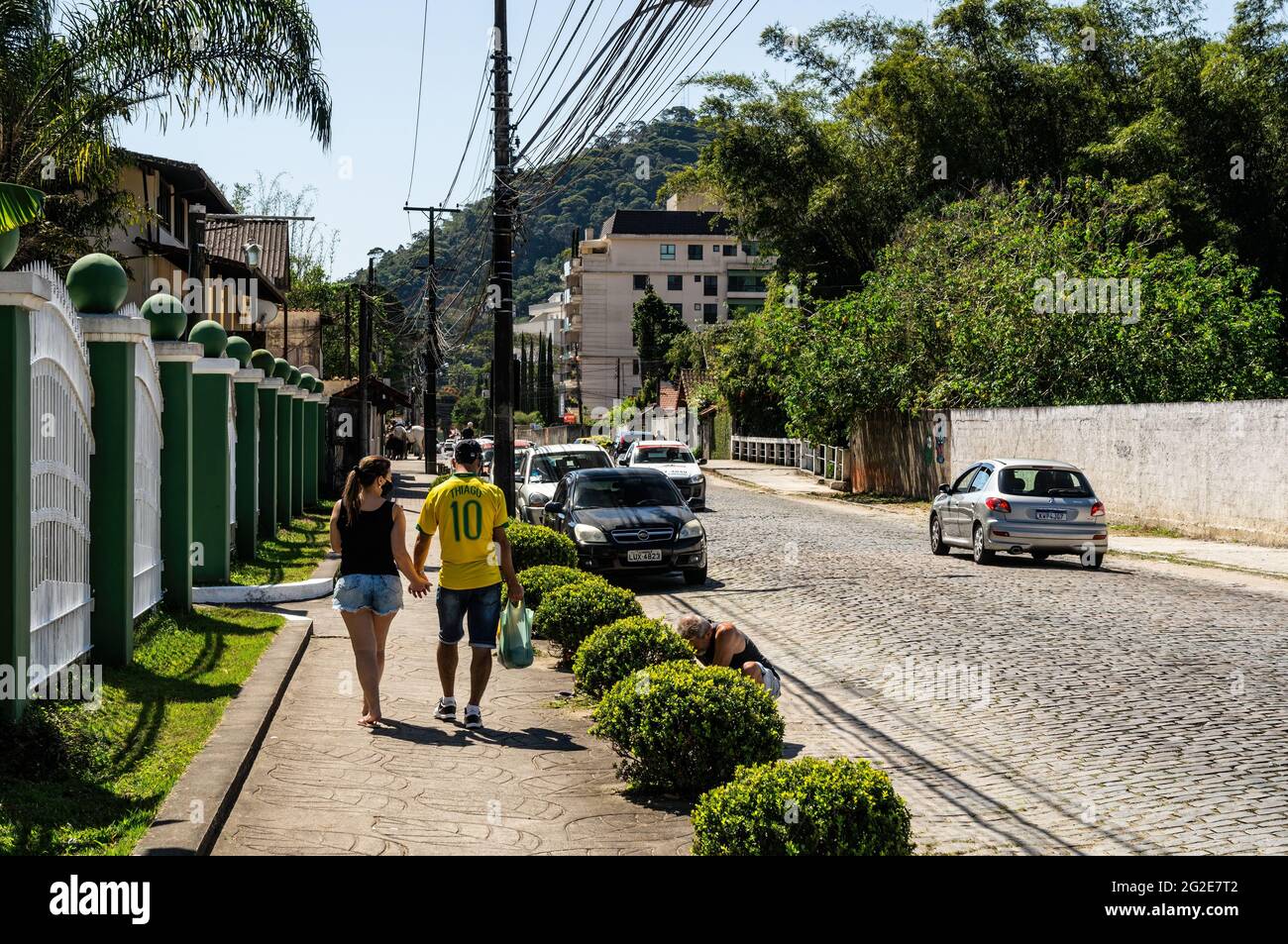 North view of Alfredo Rebelo Filho street with some local traffic passing by and a couple holding hands walking on the left sidewalk in a sunny day. Stock Photo
