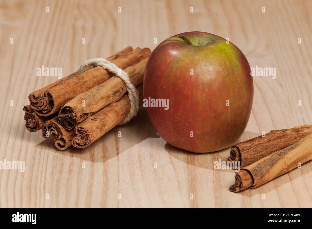 Red apple with a cinnamon stick; photo on wooden background. Stock Photo