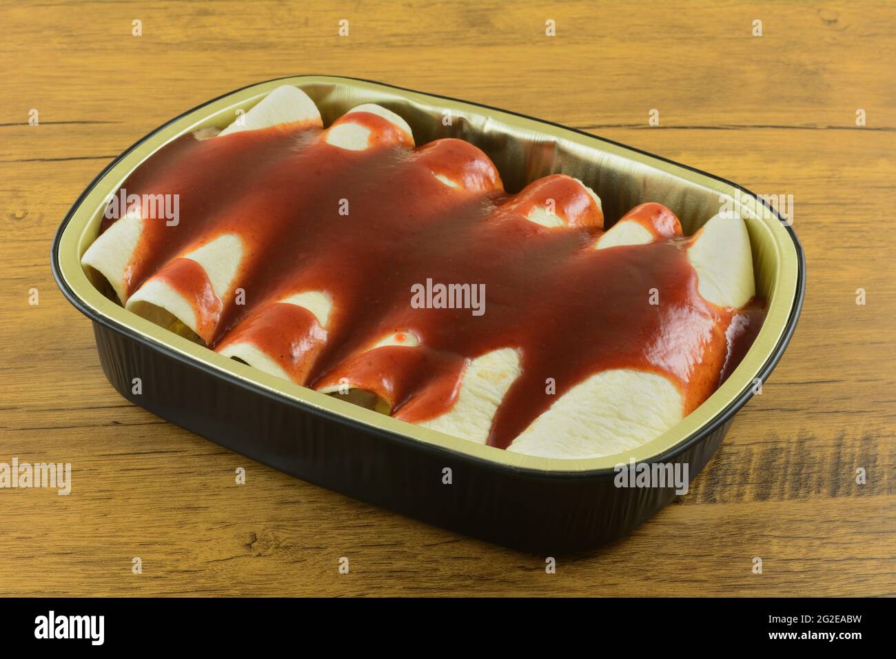 Foil pan full of uncooked enchiladas covered in red enchilada sauce Stock Photo