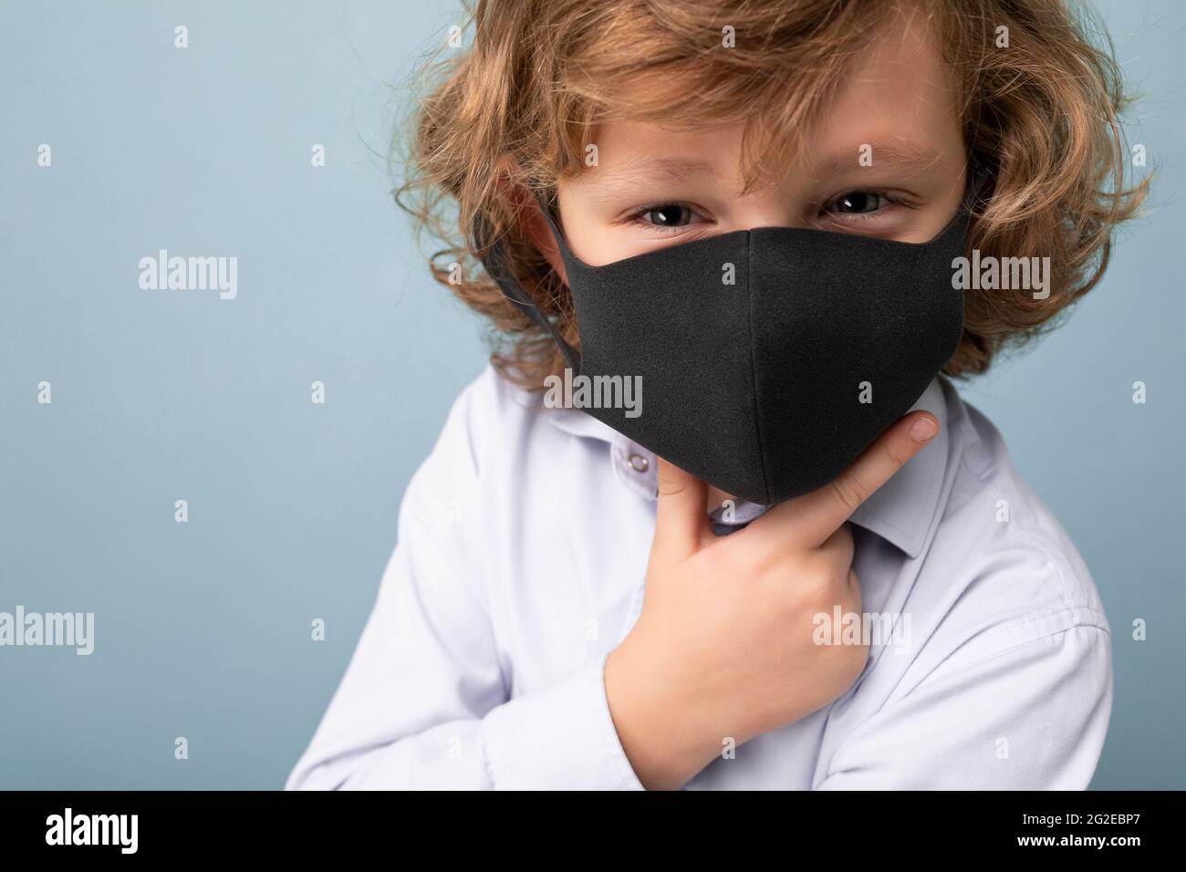 Closeup photo of handsome curly blonde little boy in medical black mask ...