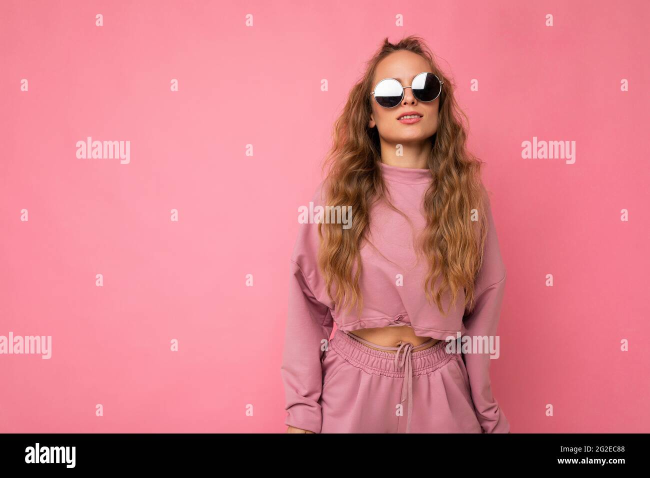 Photo shot of beautiful young dark blonde woman wearing casual clothes and stylish sunglasses isolated over colorful background looking at camera Stock Photo