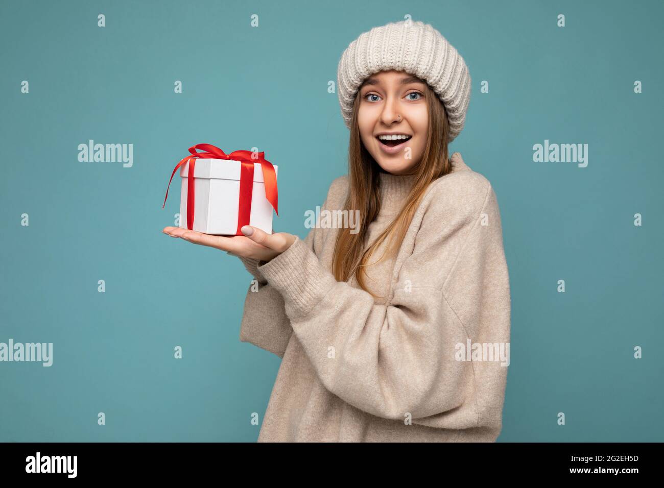 Photo shot of pretty positive surprised young dark blond woman isolated over colourful background wall wearing trendy winter outfit holding gift box Stock Photo