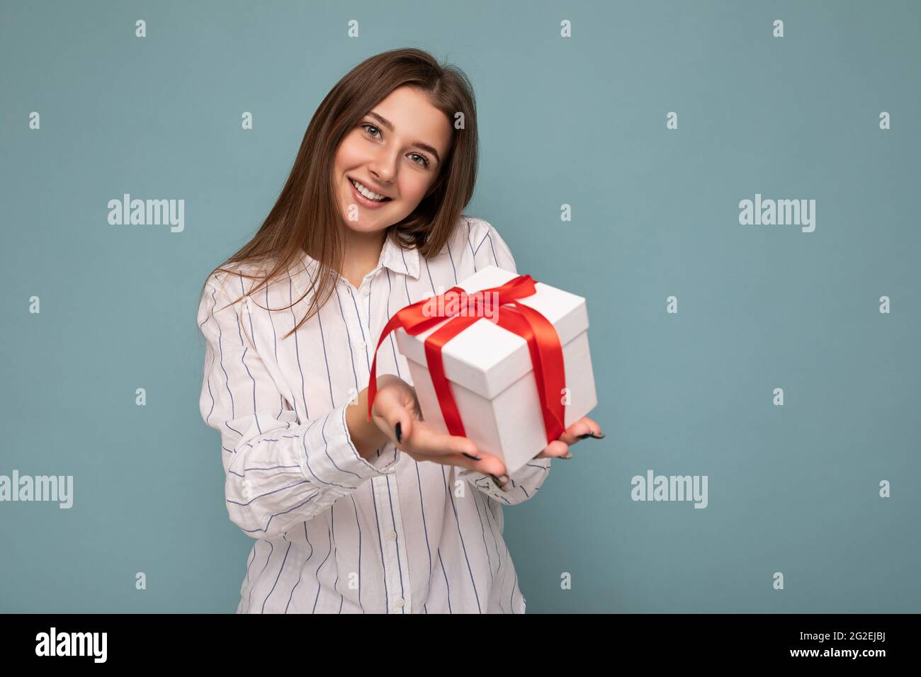 Beautiful happy young dark blonde woman isolated over colourful background wall wearing stylish casual clothes holding gift box and looking at camera Stock Photo