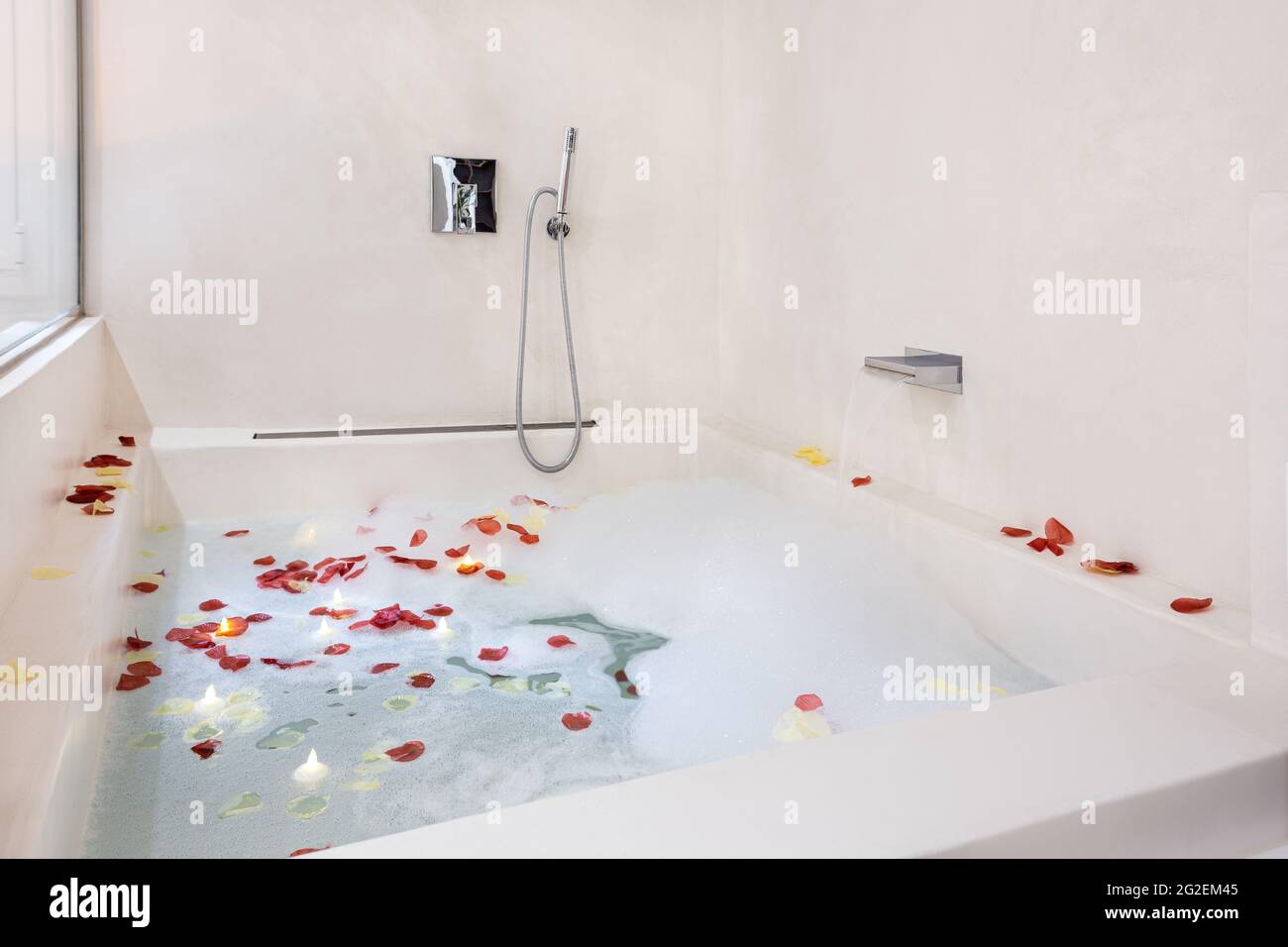 Rose petals put in bathtub for romantic bathroom atmosphere. Bubble bath arranged for honeymoon