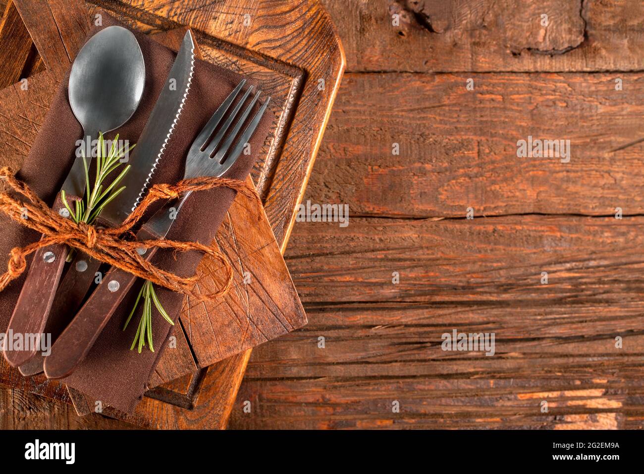 Spoon, fork and knife, restaurant cutlery, on a brown linen napkin, on rustic wooden background Stock Photo