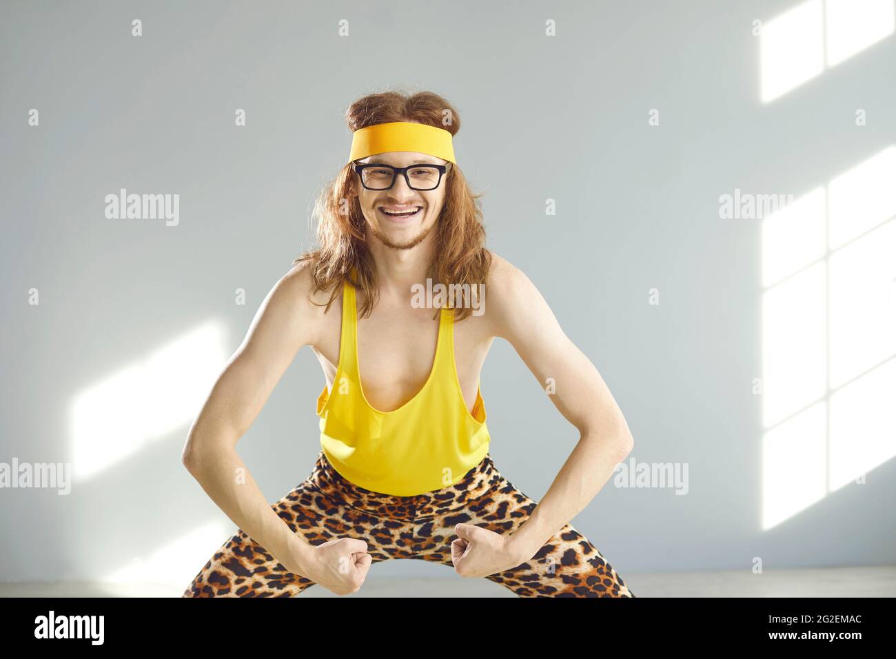Happy skinny man in funny retro activewear smiling and showing his weak arm muscles Stock Photo
