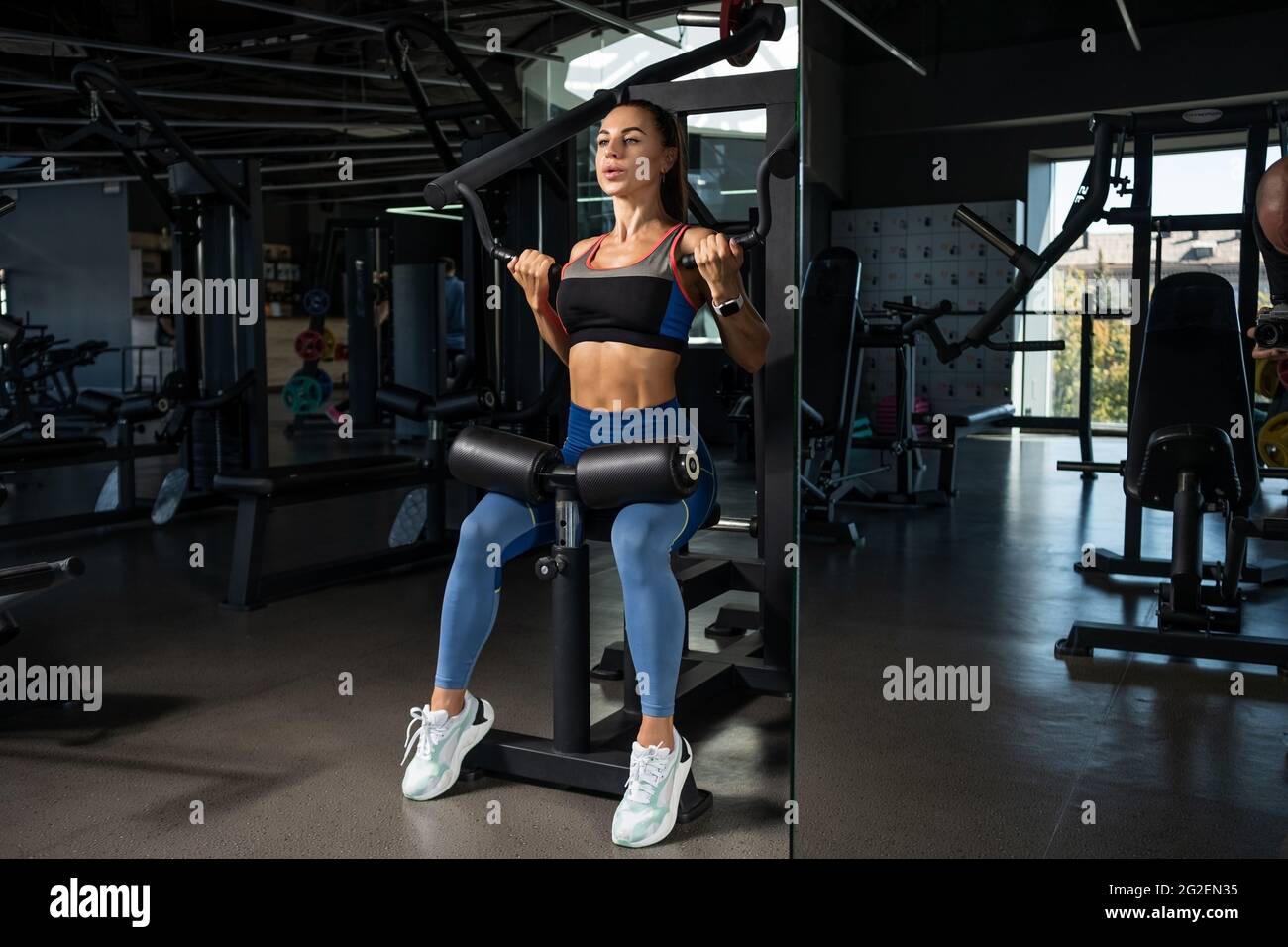 Girl doing exercises for back muscles on strength machine at gym Stock Photo