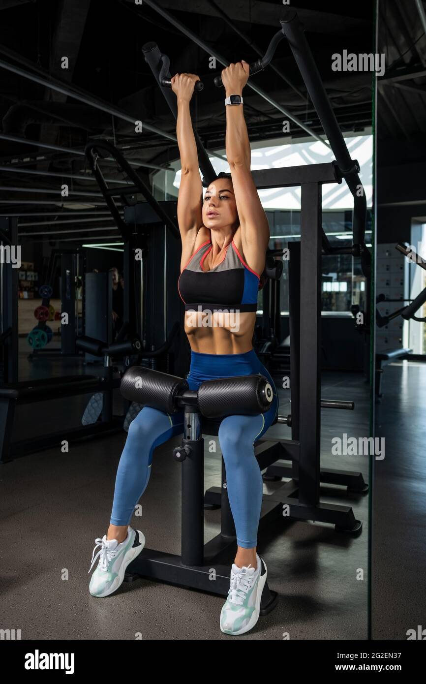 Girl doing reverse grip high lever row on strength machine at gym Stock Photo