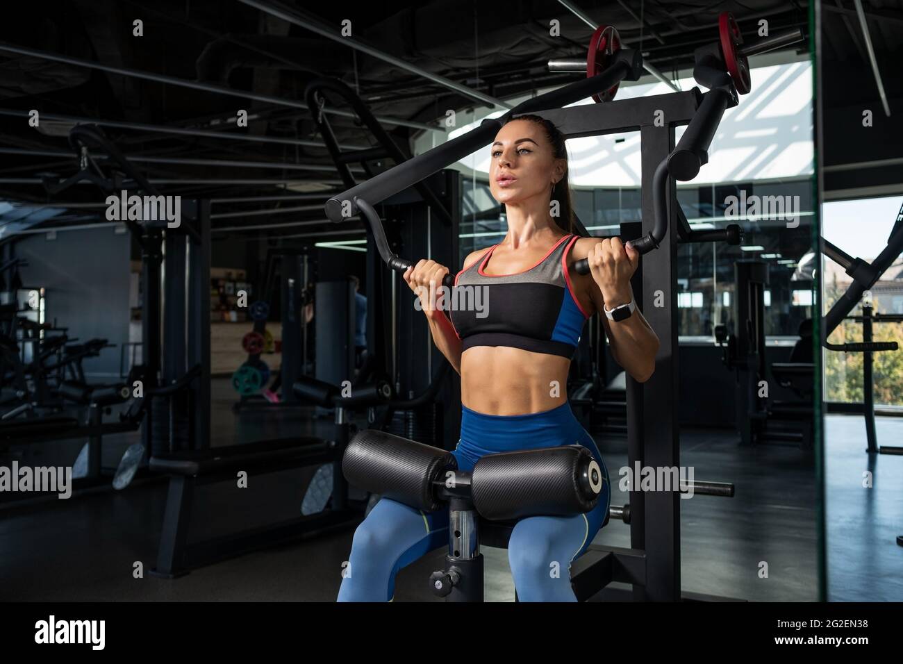 Girl doing exercises for back muscles on strength machines at gym Stock Photo