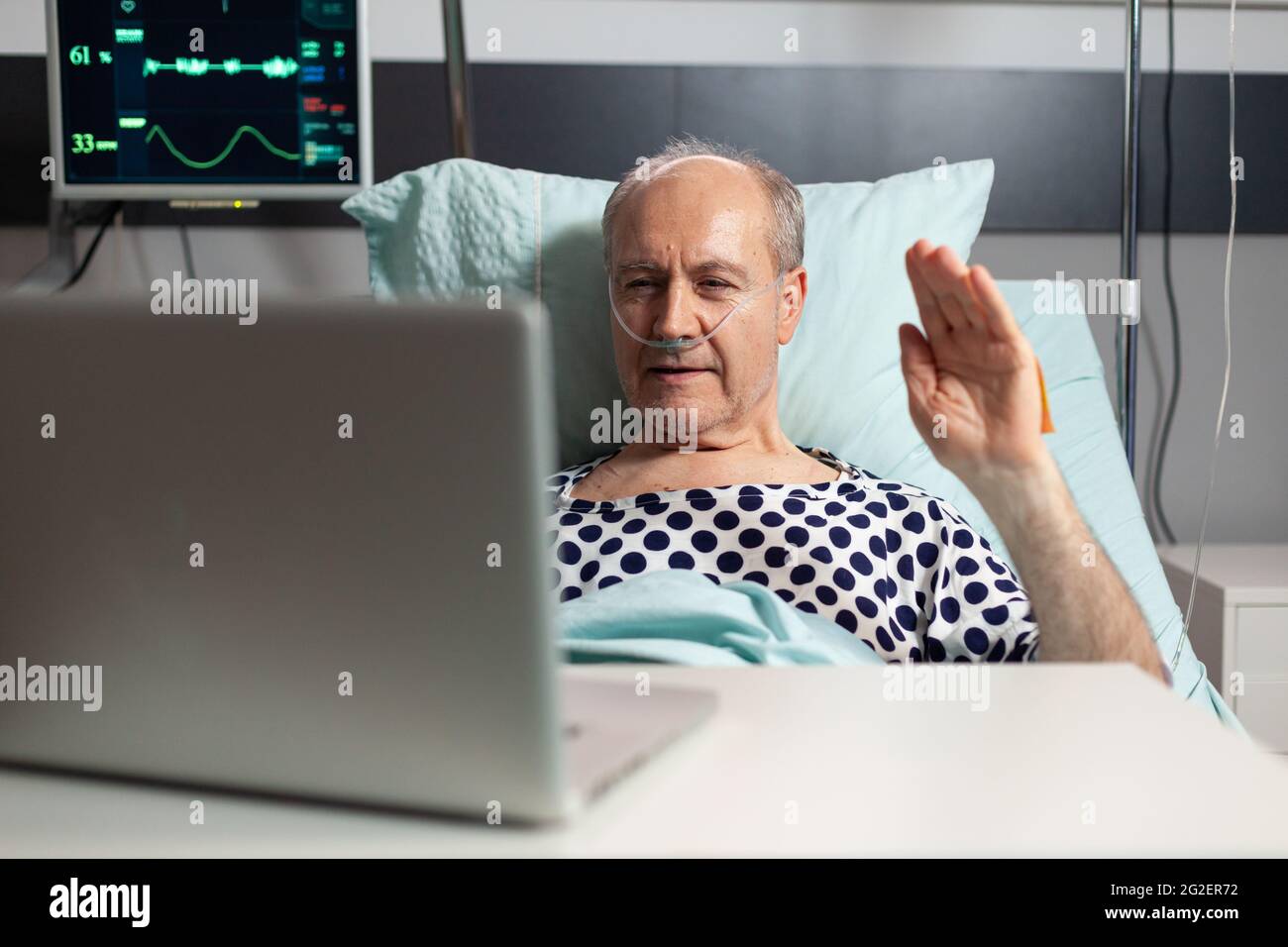 Cheerful sick senior man waving at camera during video conference using