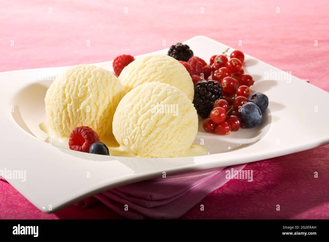 three scoops of vanilla icecream and various berry fruit on white plate Stock Photo