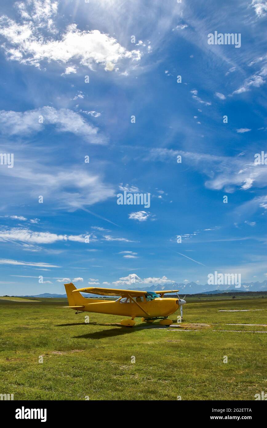 Small plane standing on a grass field against Tatra Mountains and blue cloudy sky Stock Photo