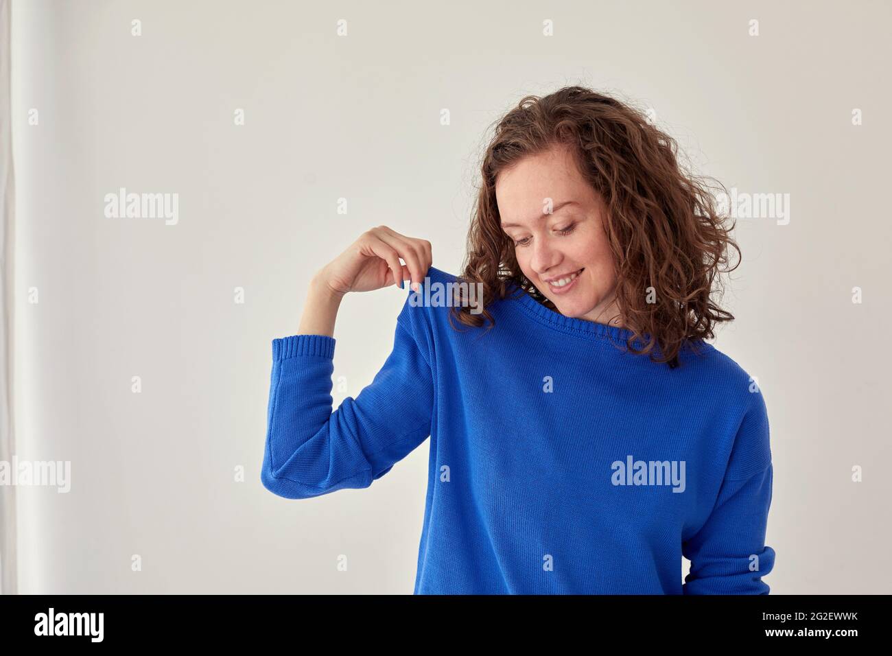 Young female model in trendy oversize blue woolen sweatshirt looking at camera against white background Stock Photo