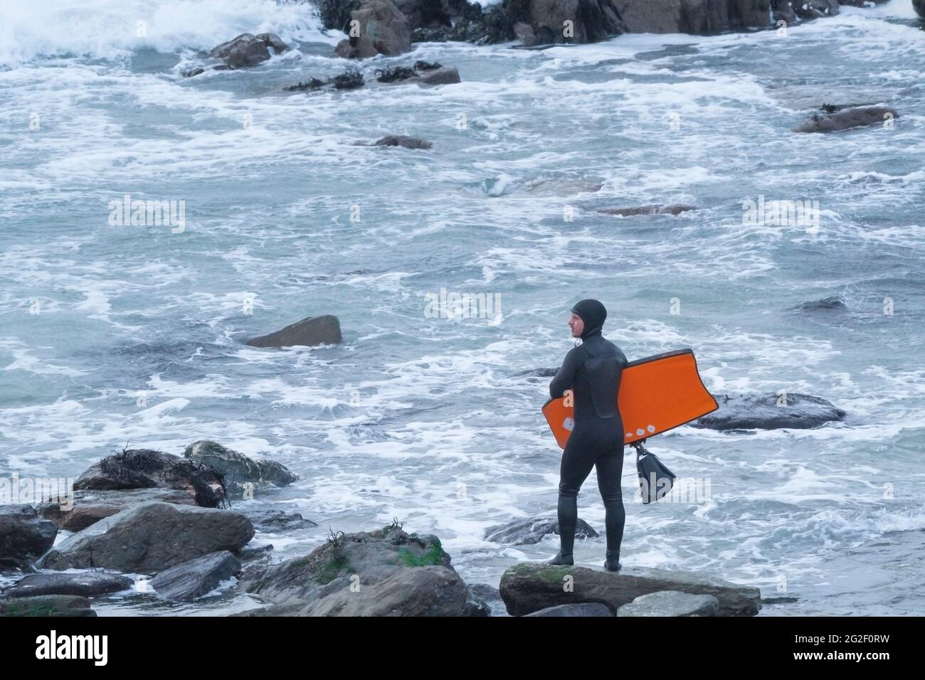 A body boarder standing on rocks at Little Fistral in Newquay in Cornwall. Stock Photo