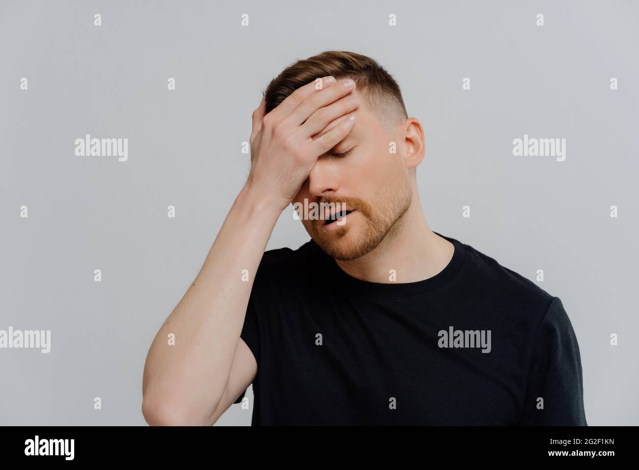 Worried man doing facepalm gesture and keeping eyes closed, concerning about troubles at work Stock Photo