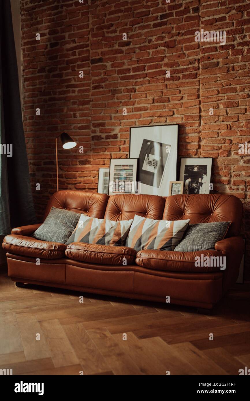 Vertical shot of a brown sofa with patterned pillows and pictures on the brick wall background Stock Photo