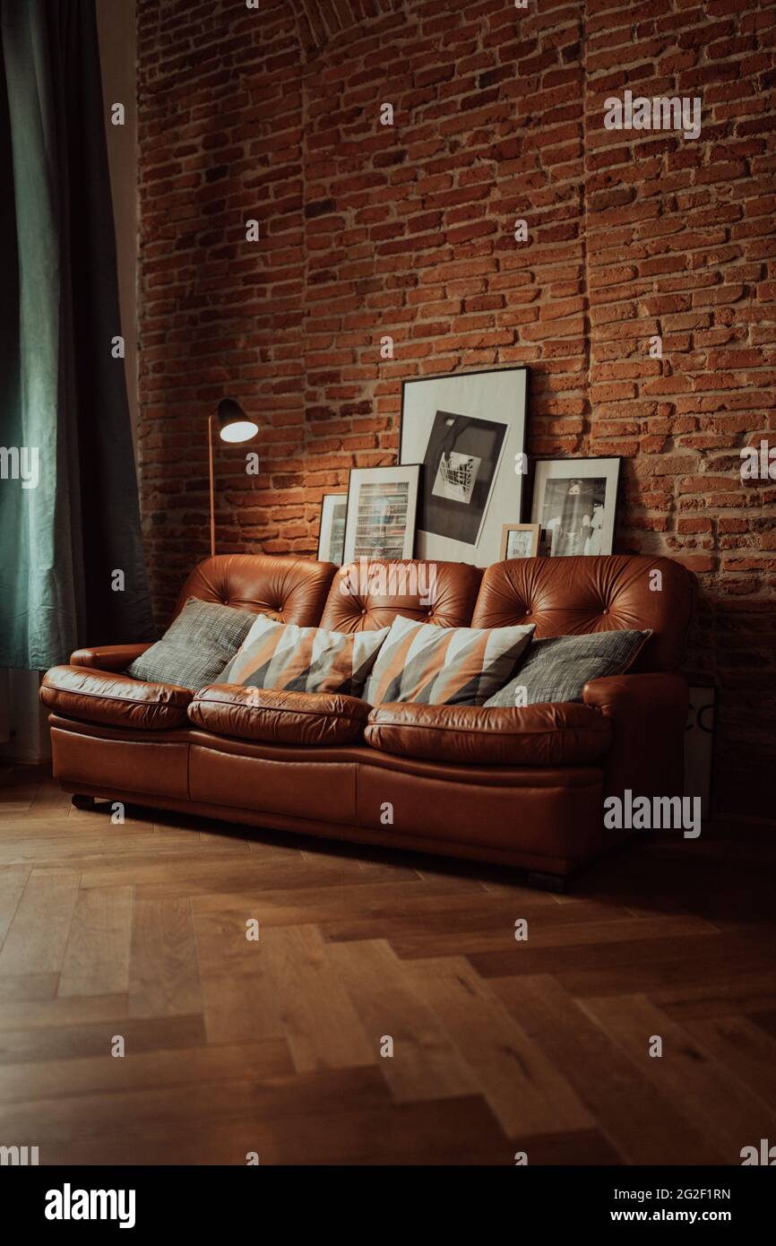 Vertical shot of a brown sofa with patterned pillows and pictures on the brick wall background Stock Photo