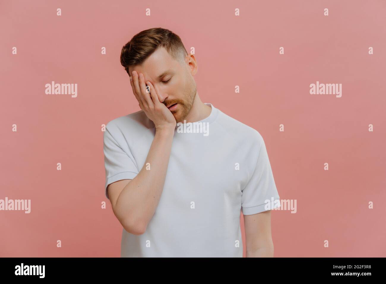 Young exhausted caucasian man posing against pink background Stock Photo