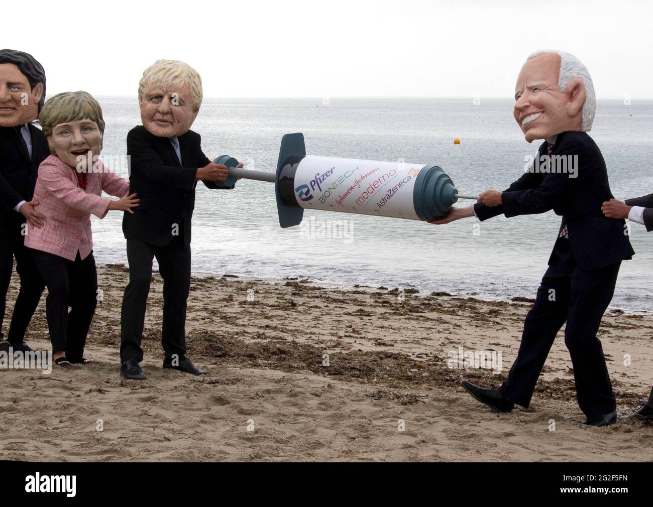 Cornwall, UK. June 11 2021: People dress up on the Swanpool beach, cornwall, as memebers of the G7 and hold a giant vaccine needle, as part of the People's Vaccine group. 11th June 2021. Anna Hatfield/Pathos Credit: One Up Top Editorial Images/Alamy Live News Stock Photo