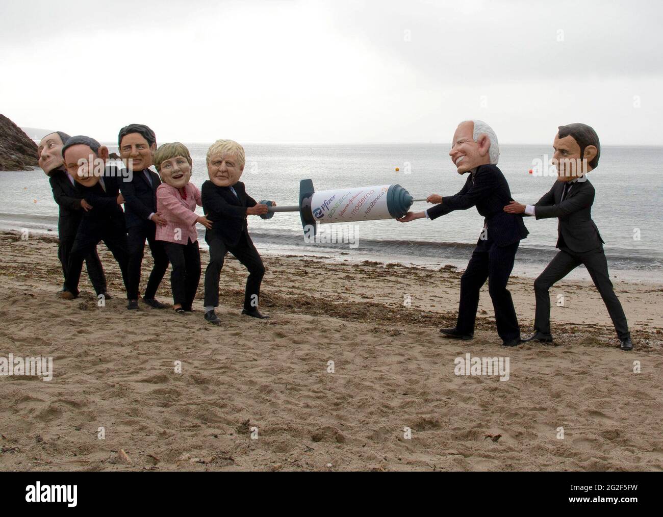Cornwall, UK. June 11 2021: People dressed as members of the G7 play tug of war with a big vaccine needle, on Swanpool beach, Cornwall. This is part of the People's Vaccine group, protesting at the G7. 11th June 2021. Anna Hatfield/Pathos Credit: One Up Top Editorial Images/Alamy Live News Stock Photo