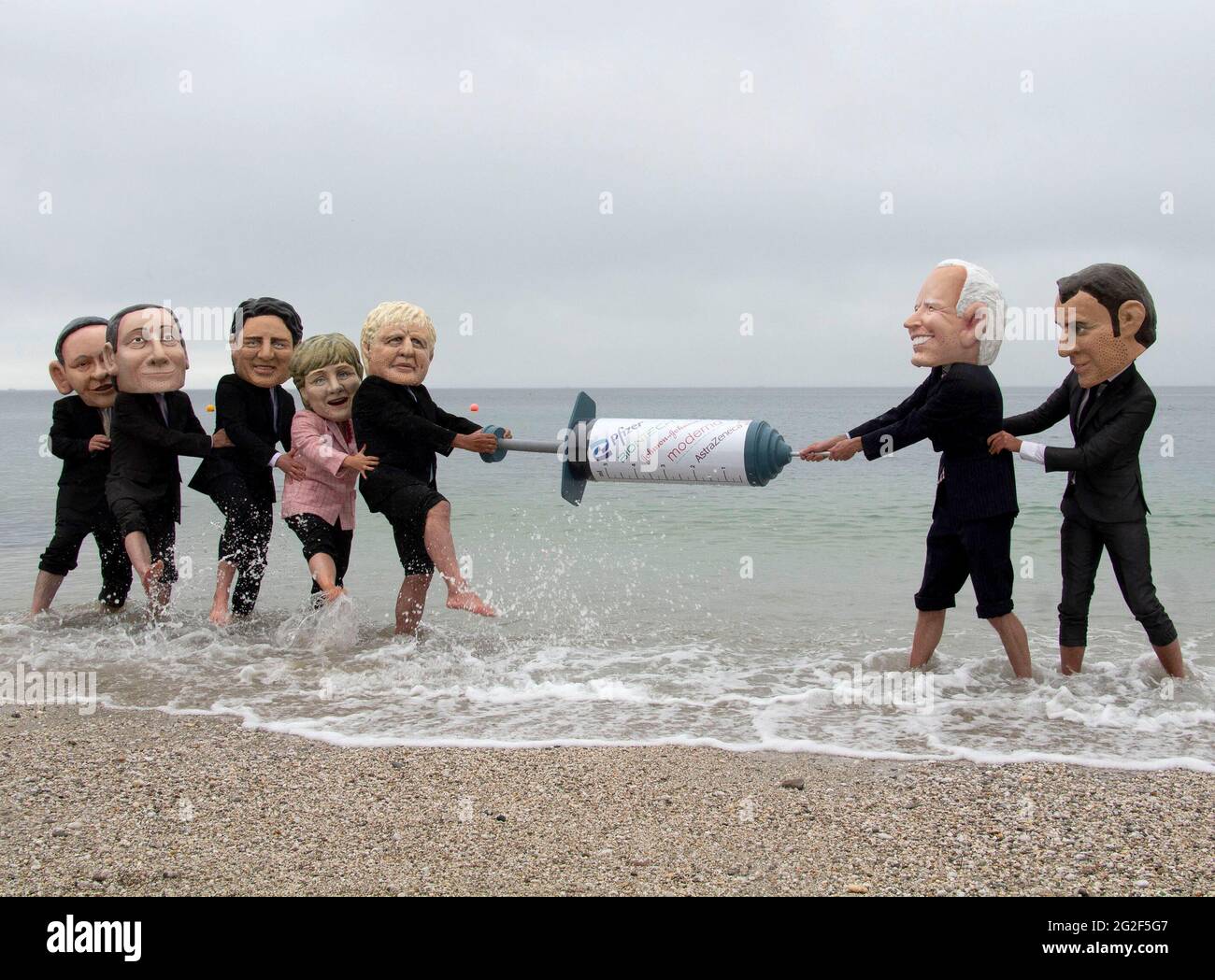 Cornwall, UK. June 11 2021: Members of the People's Vaccine group dress up as G7 leaders and splash each other in the sea at Swanpool, Cornwall. The costumed protesters also hold a big vaccine needles between them. 11th June 2021. Anna Hatfield/Pathos Credit: One Up Top Editorial Images/Alamy Live News Stock Photo