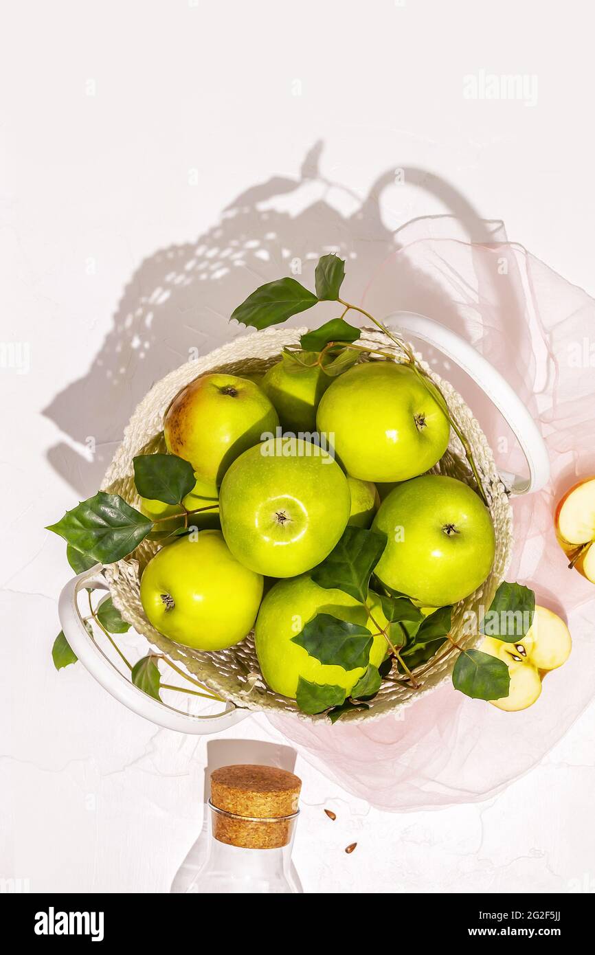 Vertical composition with green apples in a wicker bag and bottle with juice on a white background. Concept of local market and farm fruits Stock Photo