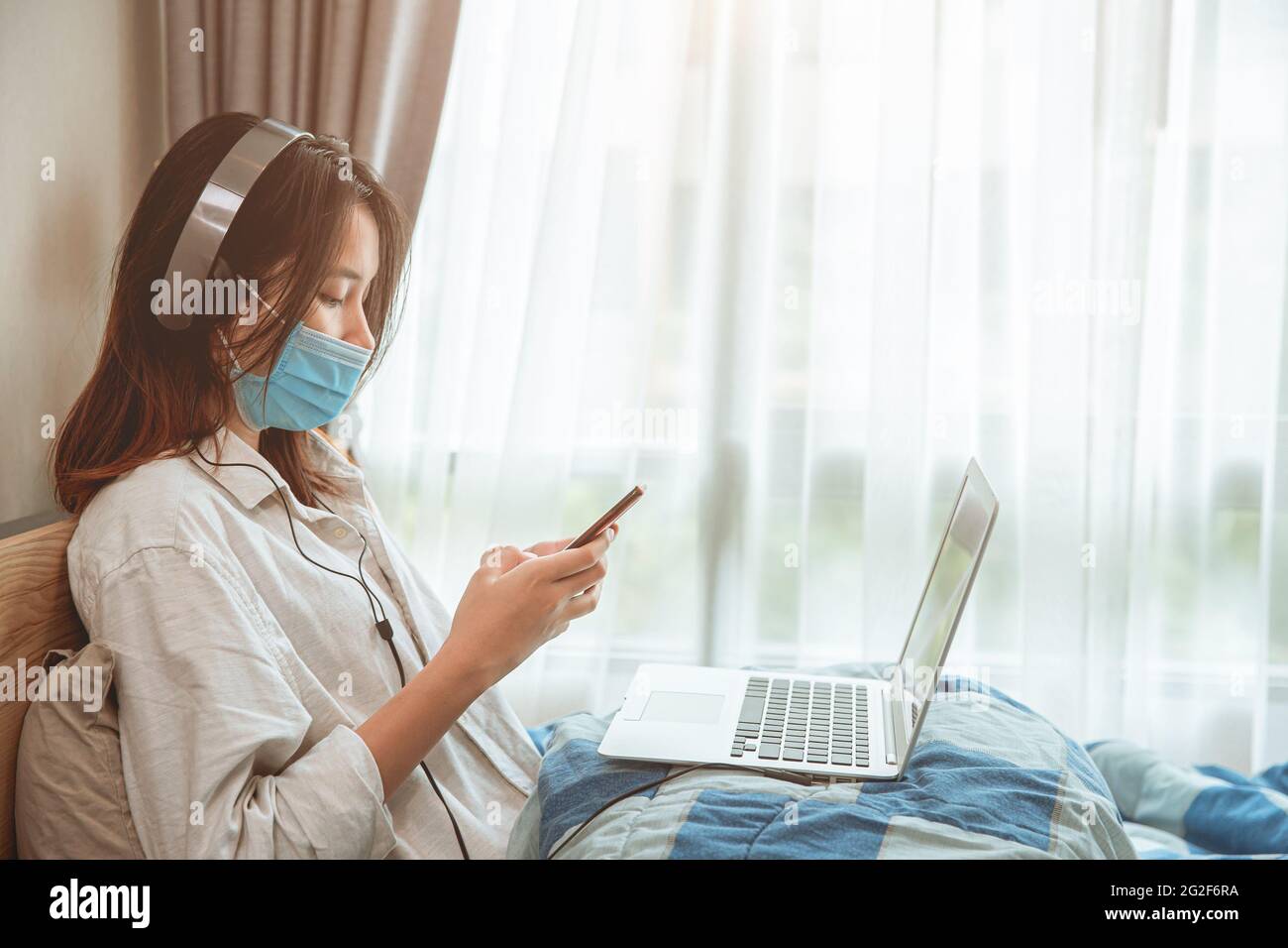 Girl teen covid self quarantine lockdown stay at home enjoy with smartphone internet laptop listening the music. Stock Photo