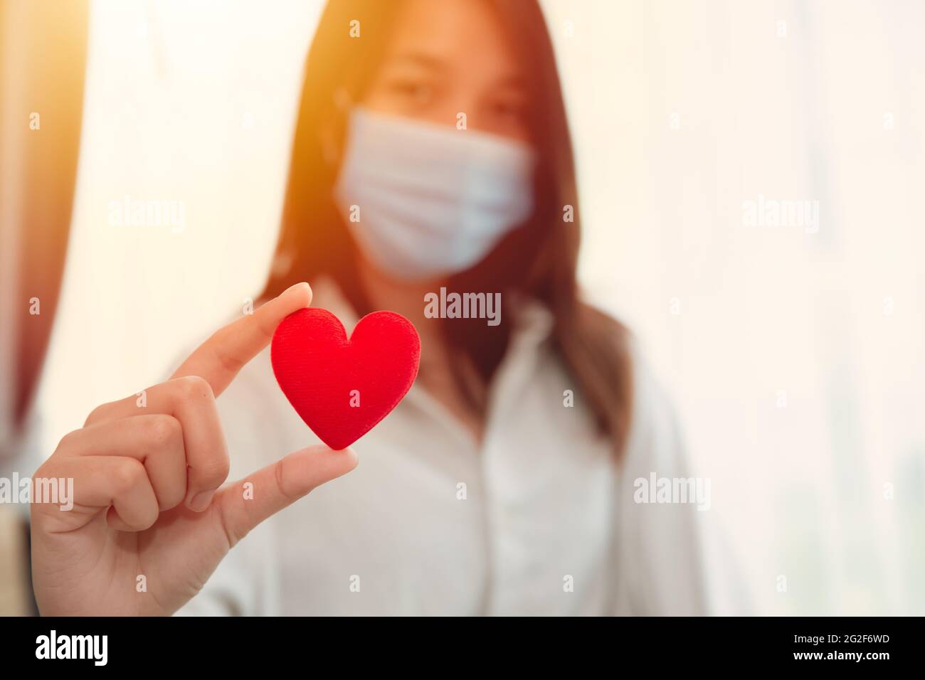 Girl teen wearing face mask hand holding red heart for love care together stay healthy and protect Covid Corona virus spreading concept. Stock Photo