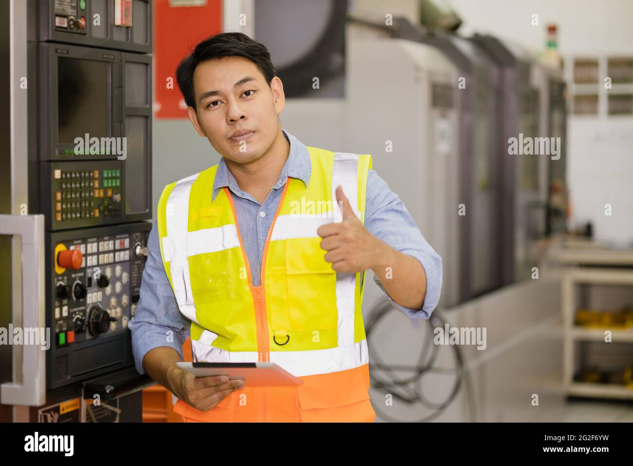 Portrait smart Asian adult professional engineer worker in factory industry CNC operator standing confident thumbs up with safety suit. Stock Photo