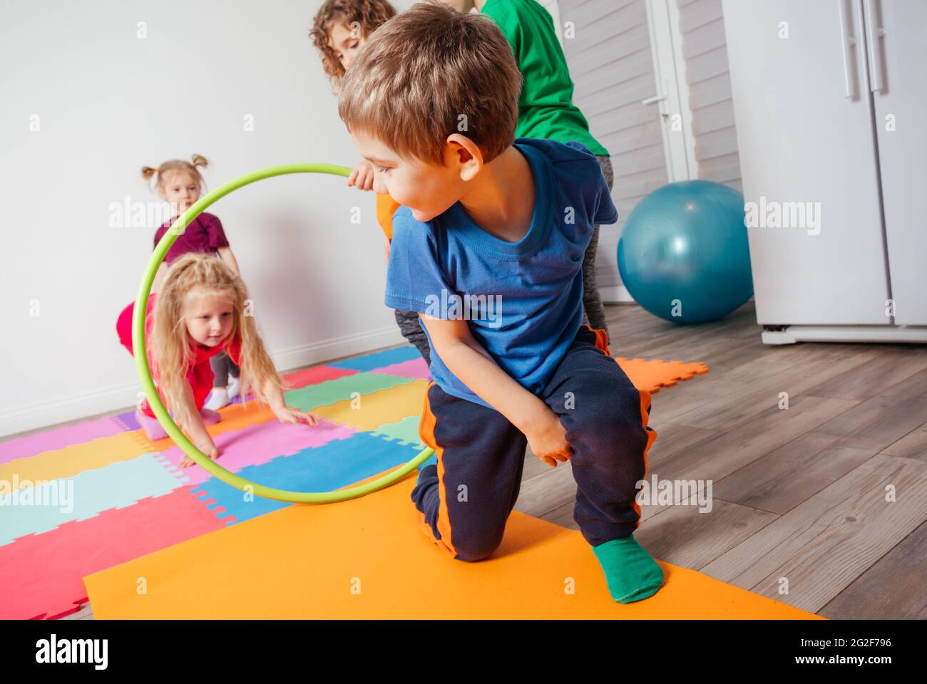 Curly girl crawling on colorful floor through hula hoops Stock Photo