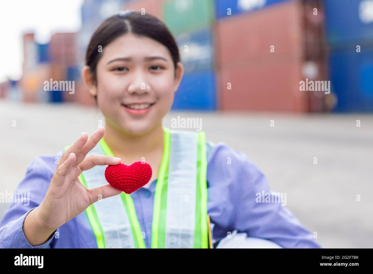 Girl teen worker in cargo container shipping port working with heart and good service mind concept. selective focus at red heart. Stock Photo