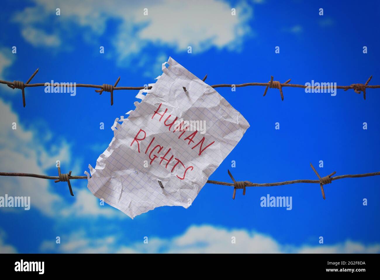 piece of paper with human rights text on barbed wire on blue sky ...