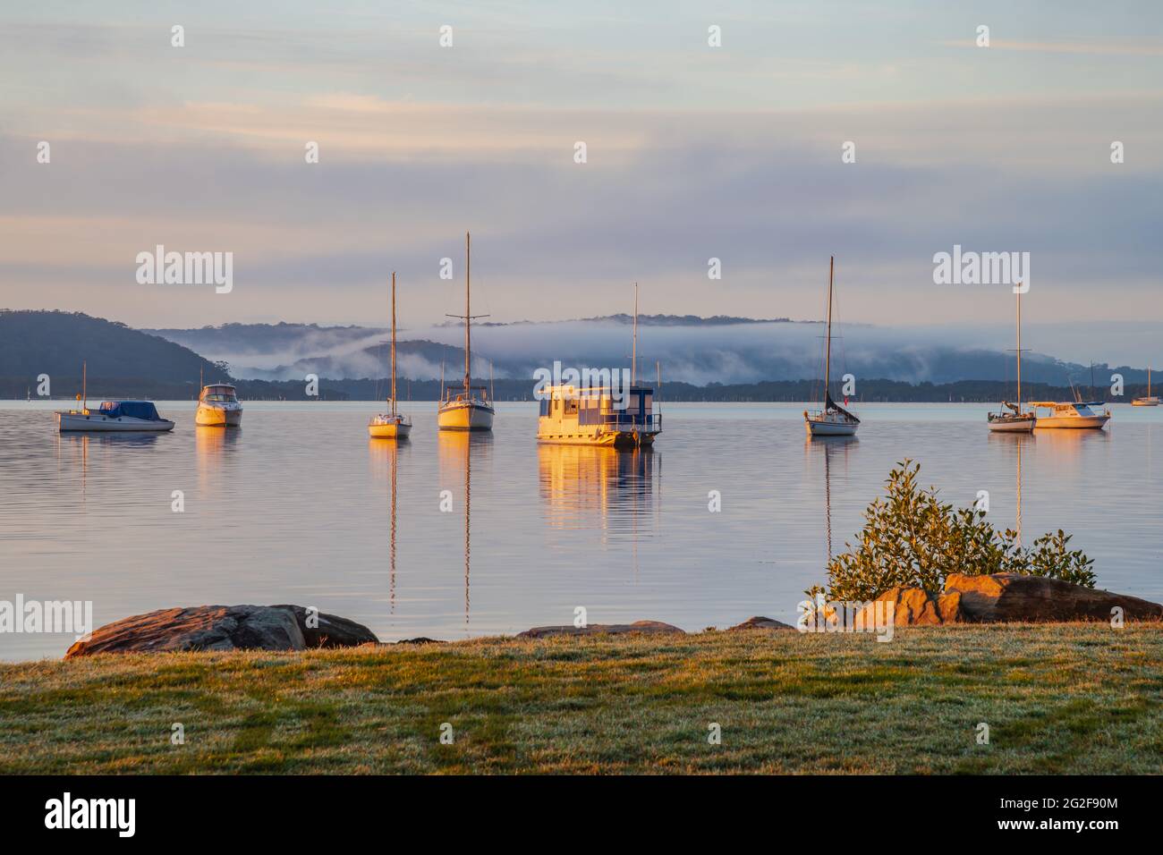 A soft pretty sunrise with boats and fog at Koolewong Waterfront on the Central Coast, NSW, Australia. Stock Photo