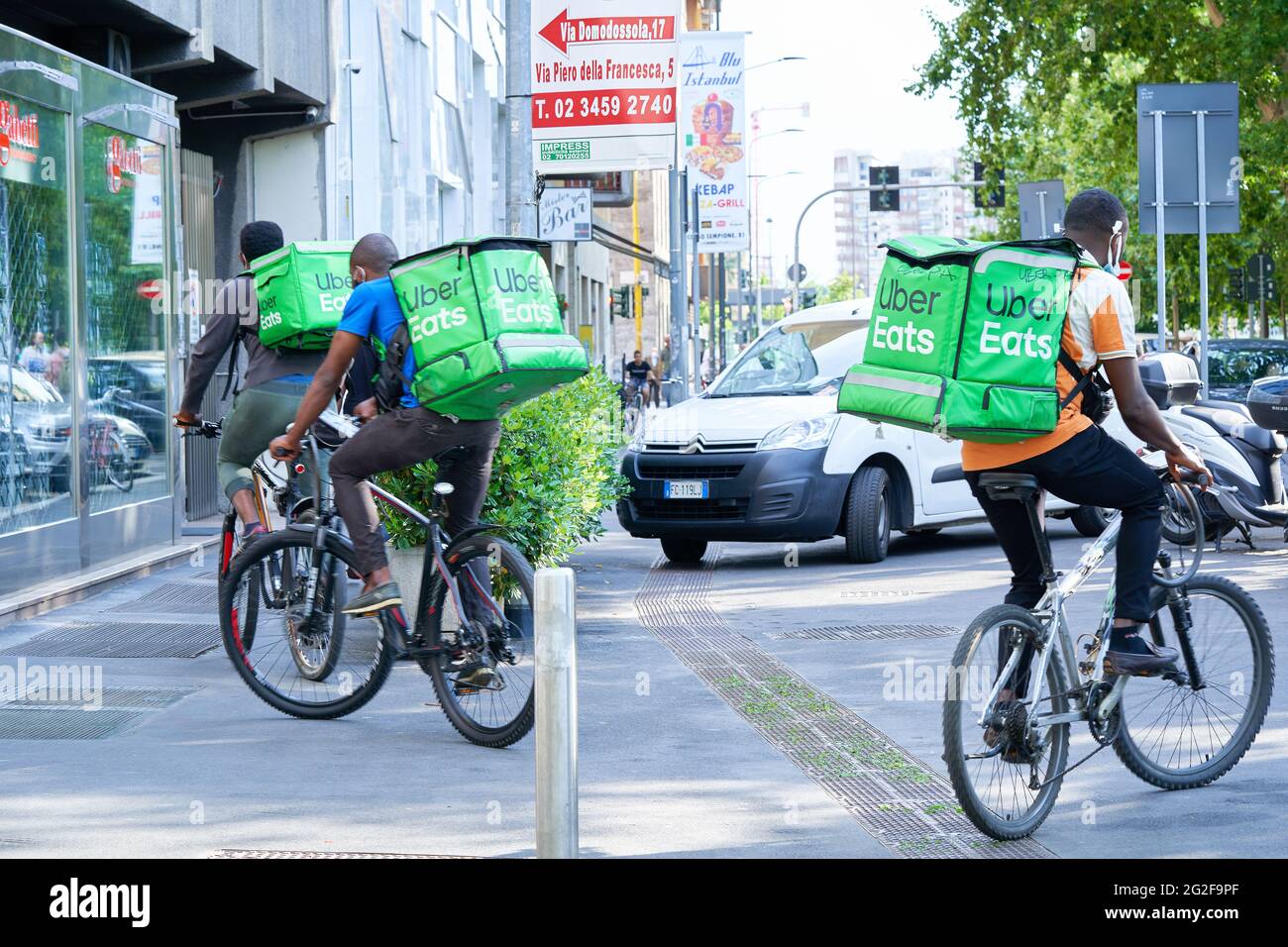 Delivery men with backpack on bicycle in the street. Courier delivering food during coronavirus pandemic. Milan, Italy - June 16, 2020 Stock Photo