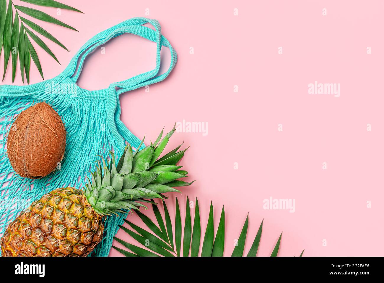 Summer pink background with pineapple, coconut and reusable net bag on pink backdrop. Stock Photo