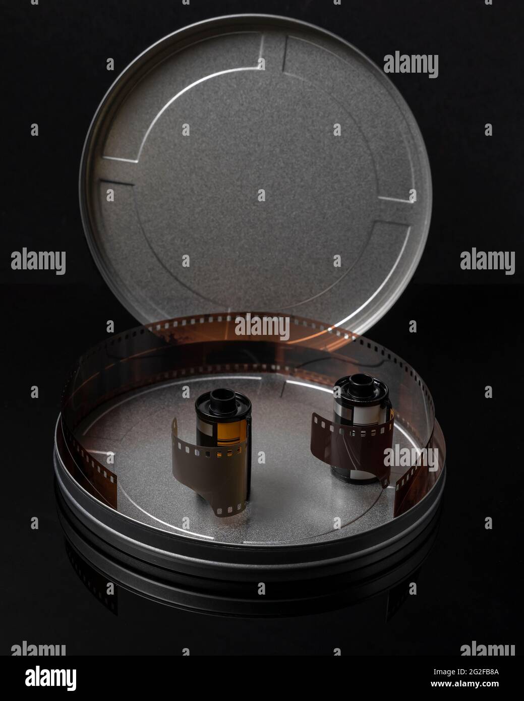 Two old rolls of analog photographic film in a circular tin container with the cap open and some negatives inside Stock Photo