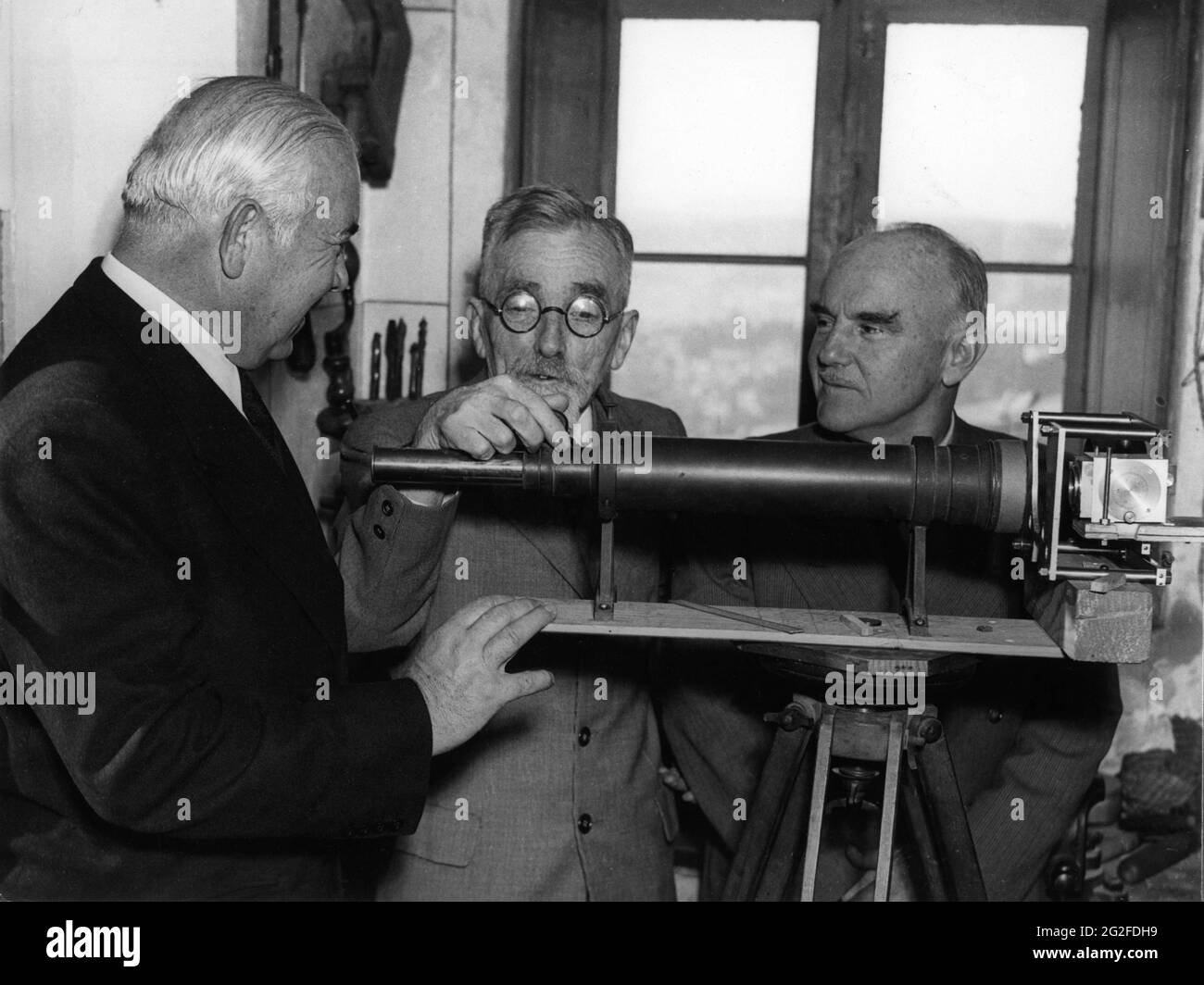 French Inventor HENRI CHRETIEN explains his Widescreen Anamorphic Lens to be used in CinemaScope Productions to President of 20th Century Fox Corporation SPYROS P. SKOURAS (at left) and Fox Research Director EARL SPONABLE (right) publicity for Twentieth century Fox Stock Photo