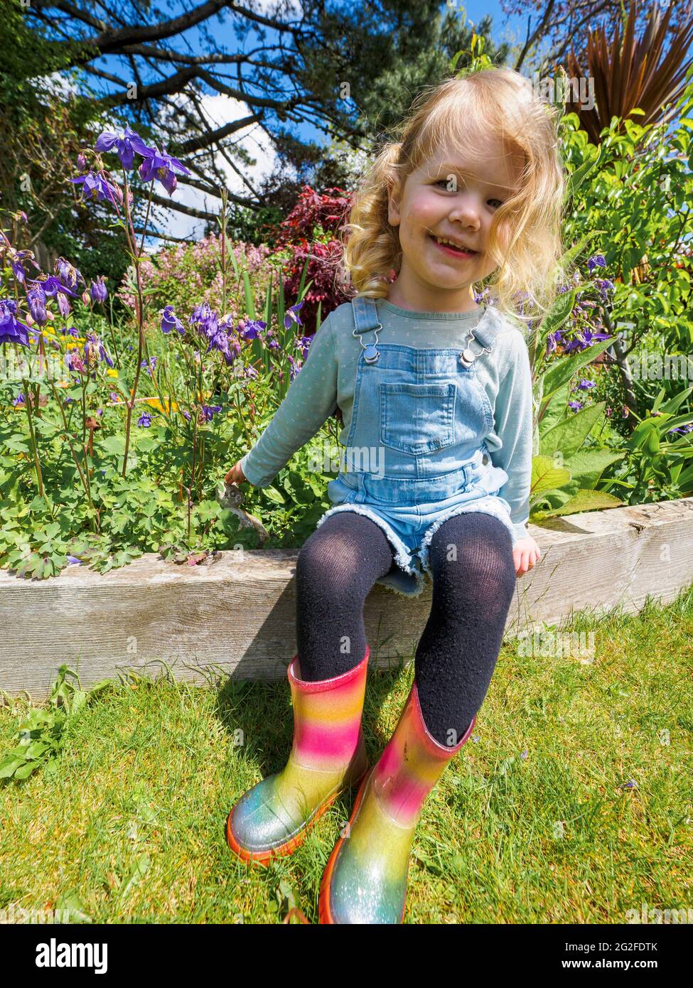 Three year old girl sat in the garden in summer, Devon, UK Stock Photo