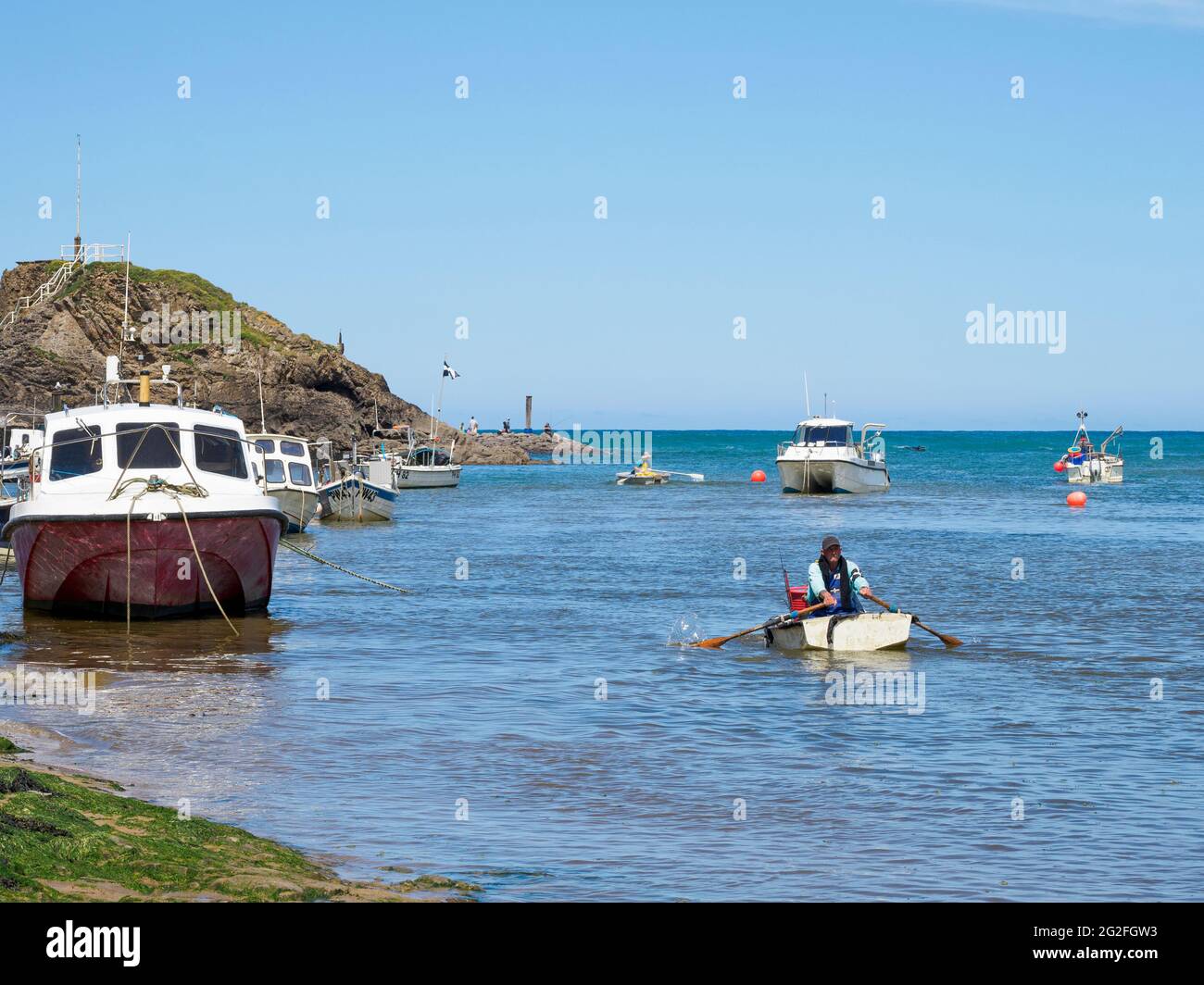 Fishermen rowing out to boats in a tidal harbour, Bude, Cornwall, UK Stock Photo