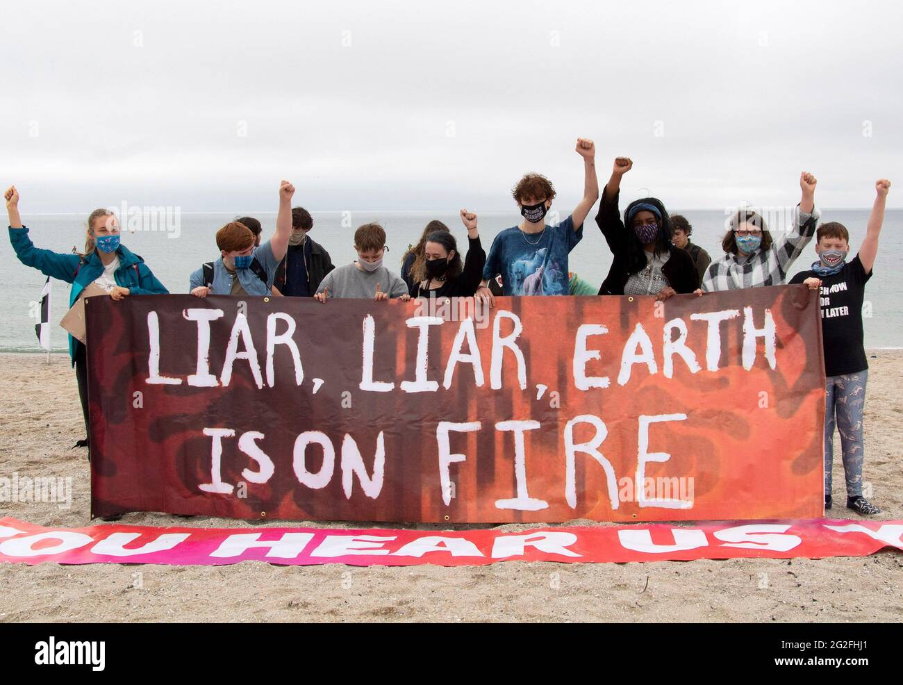 Cornwall, UK. June 11 2021: Climate strikers come together on Gyllyngvase beach as the G7 begins in Cornwall the same weekend. the strikers stand with raised fists behind a banner that reads 'Liar Liar earth is on fire' 11th June 2021. Anna Hatfield/Pathos Credit: One Up Top Editorial Images/Alamy Live News Stock Photo