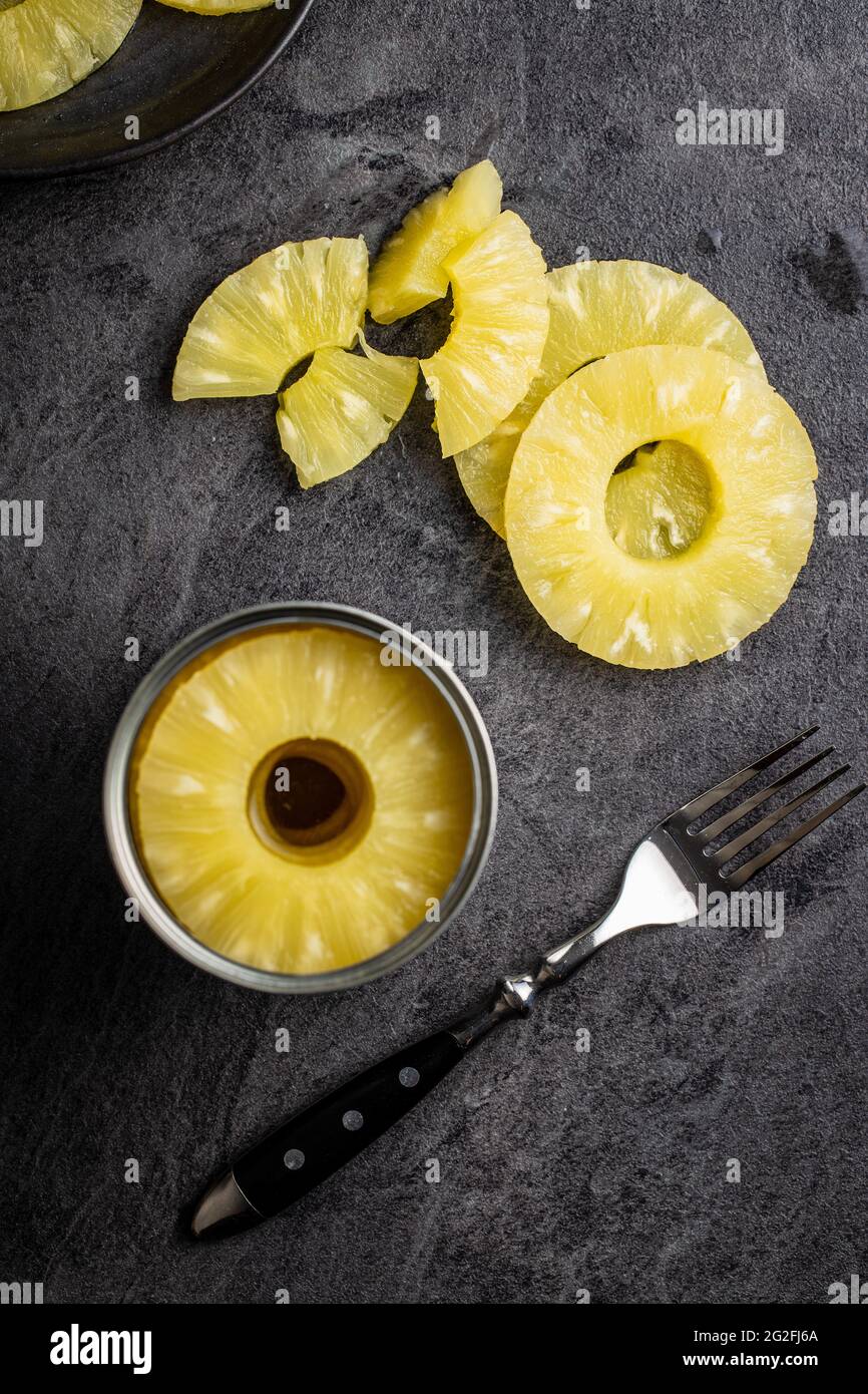 Canned sliced pineapple fruit on black table. Top view. Stock Photo