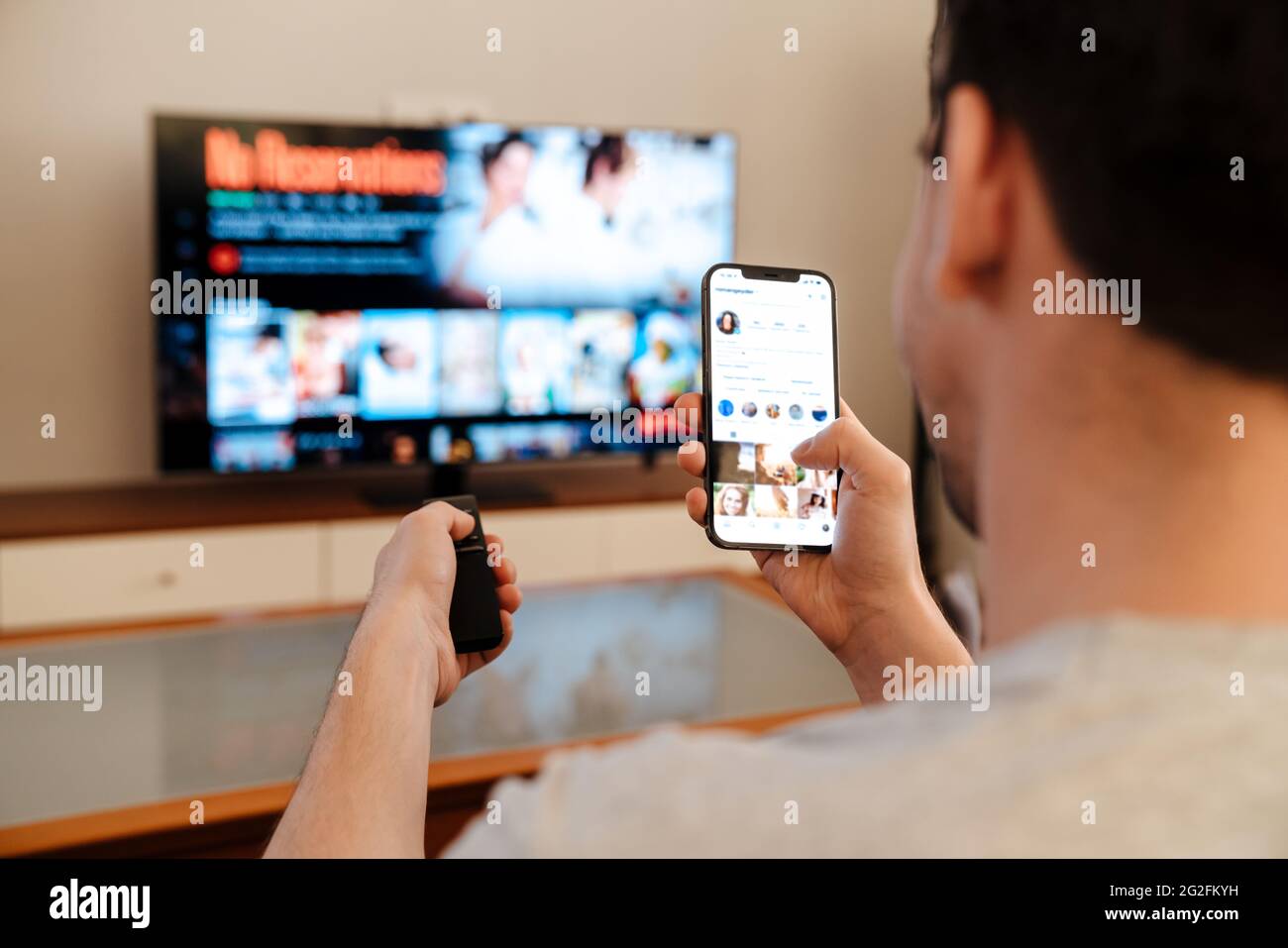 Caucasian guy using mobile phone while watching TV at home Stock Photo