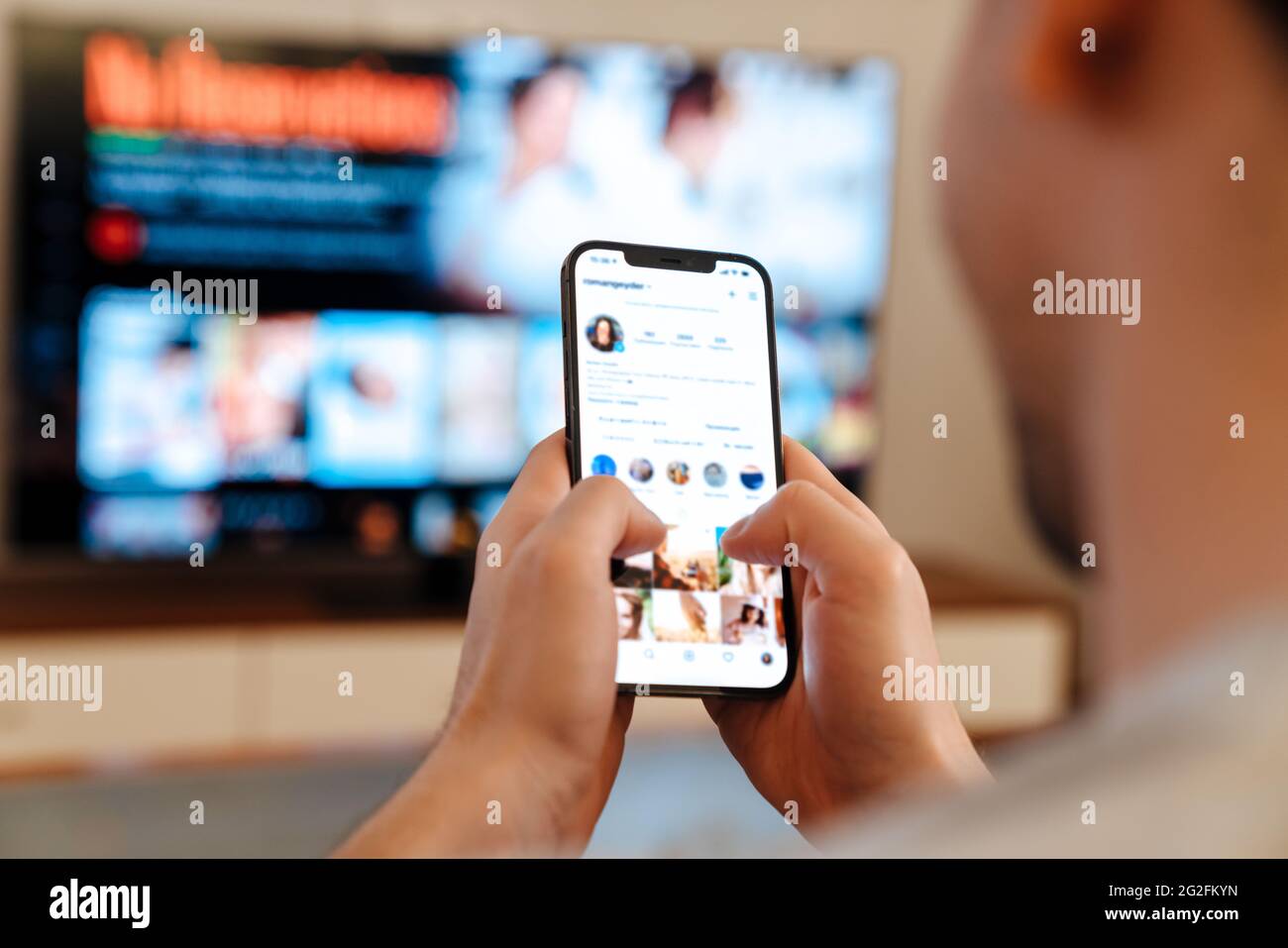 Caucasian guy using mobile phone while watching TV at home Stock Photo