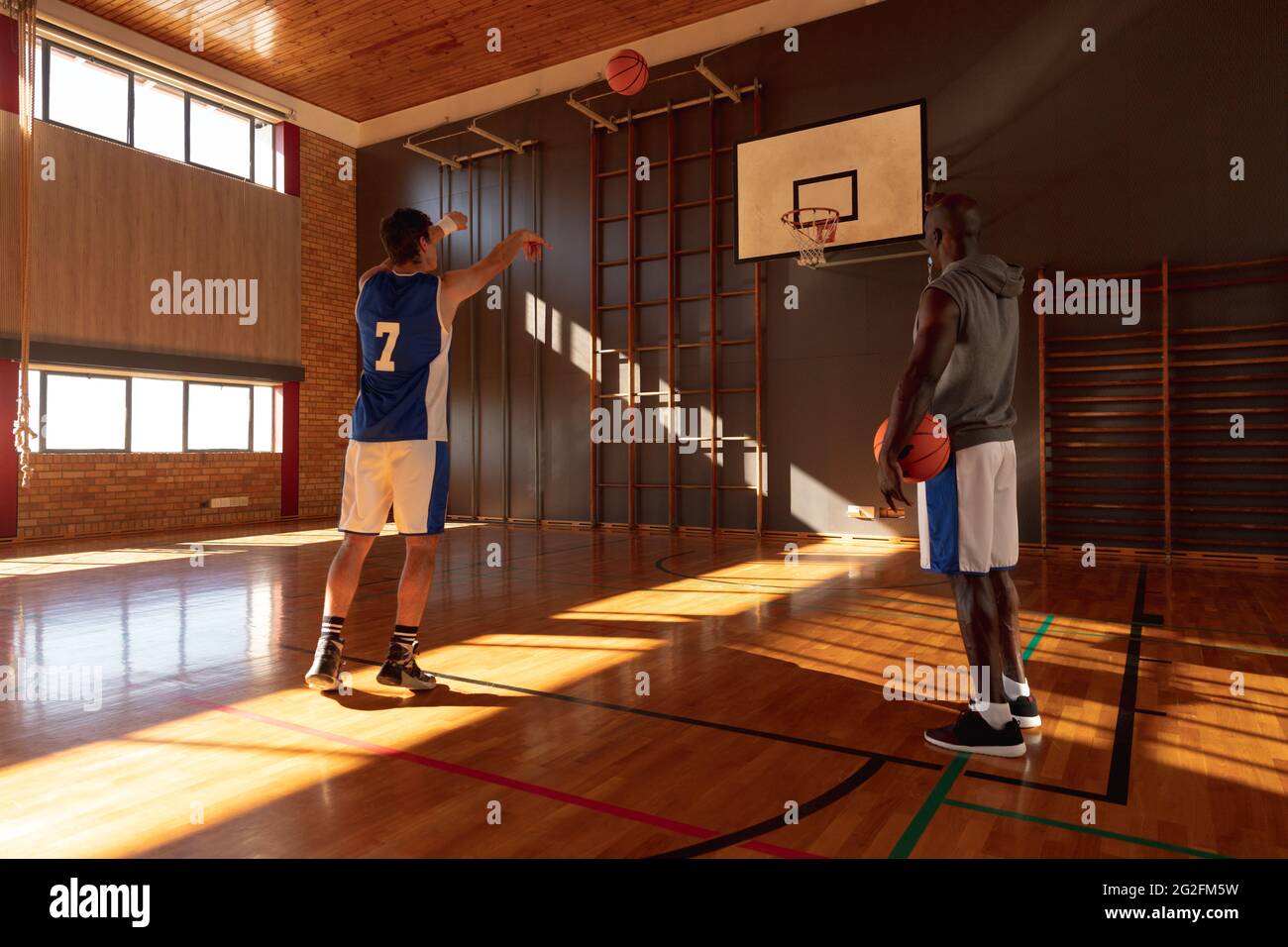 Caucasian male basketball player and coach practicing shooting with