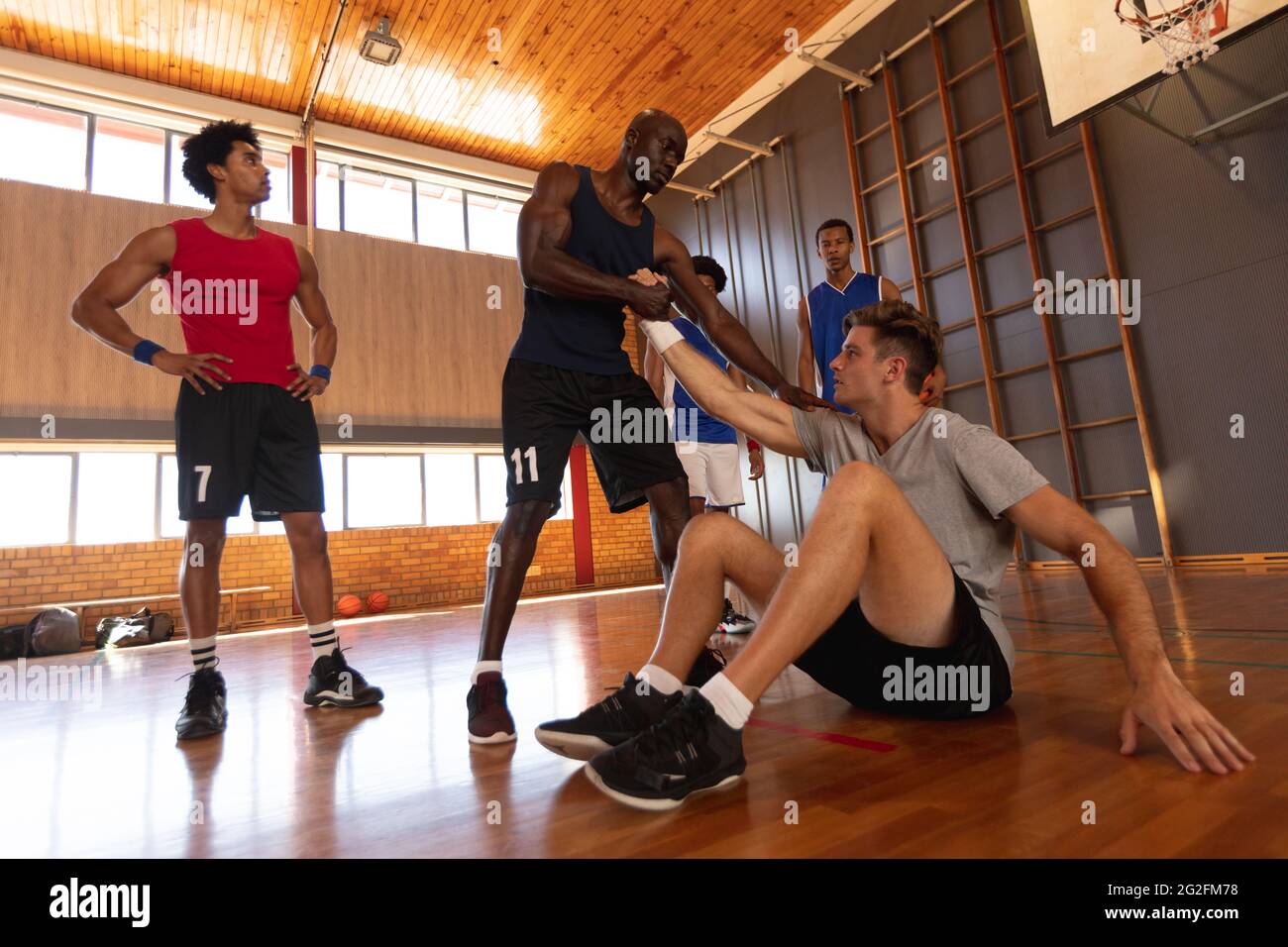 Diverse male basketball team and coach helping other player Stock Photo