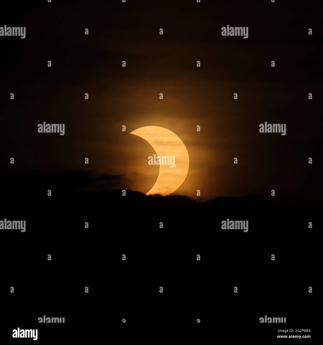 Above a layer of clouds, a partial solar eclipse is seen at sunrise