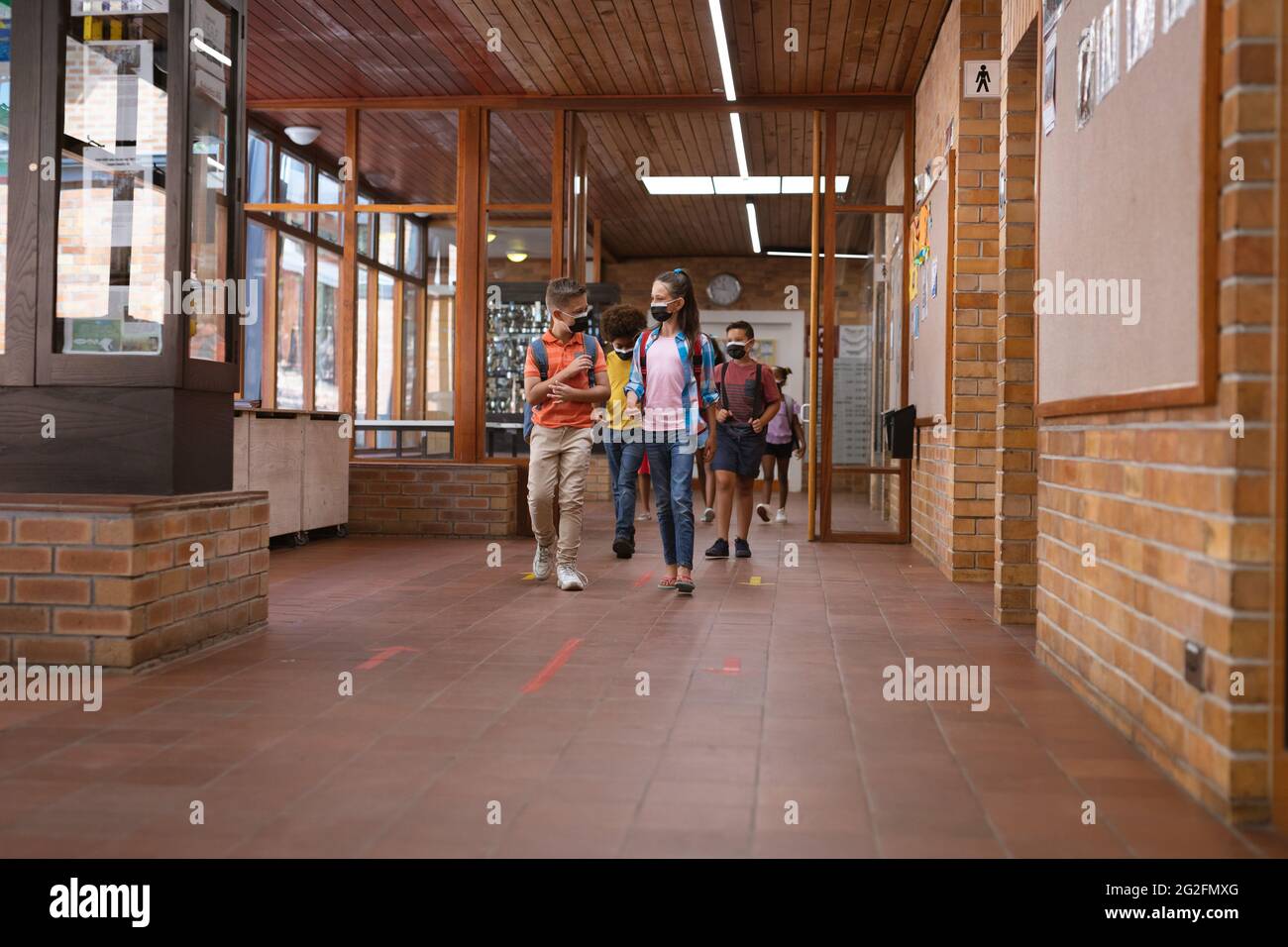 Group of diverse students wearing face masks walking in the corridor at school Stock Photo