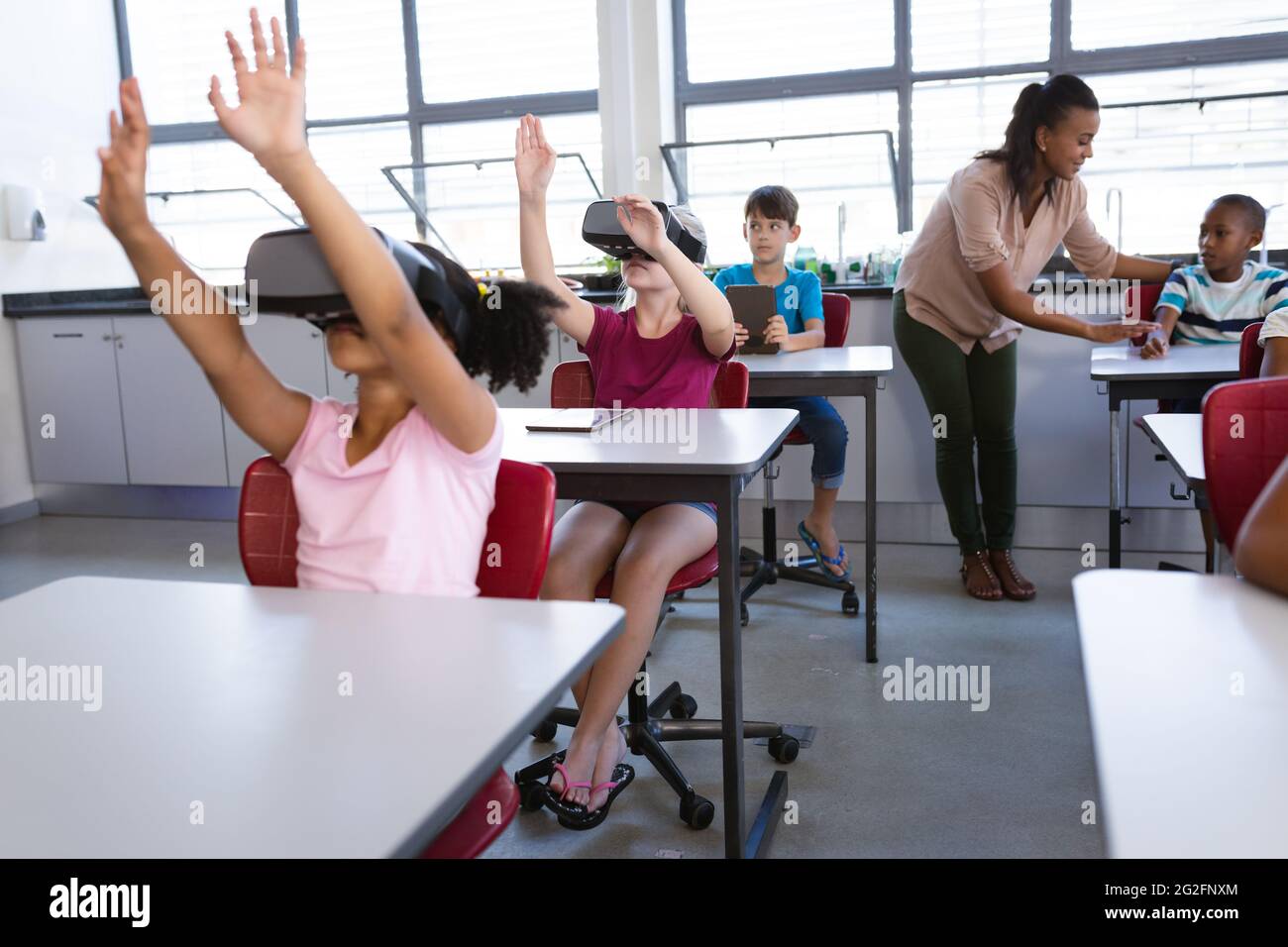 Group of diverse students using electronic devices while sitting on their desk in class at
